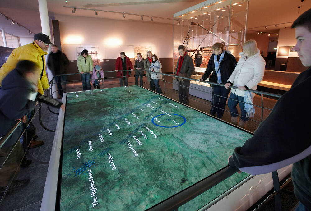 A large table showing a map of the battlefield at Culloden. People stand around the outside, looking down at it.