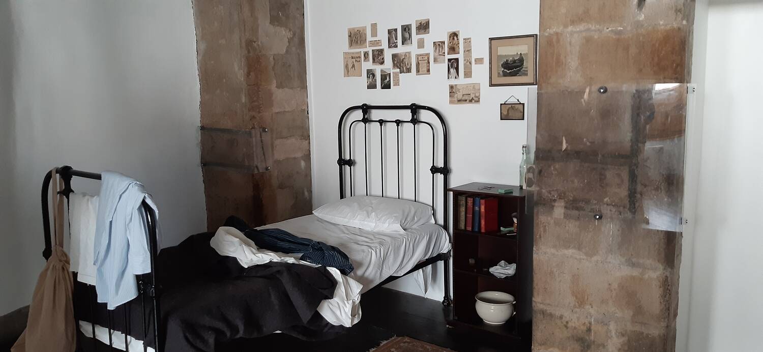 An example of a working class person’s unmade bed at Gladstone’s Land, with old sepia postcards and photographs stuck to the wall above it.