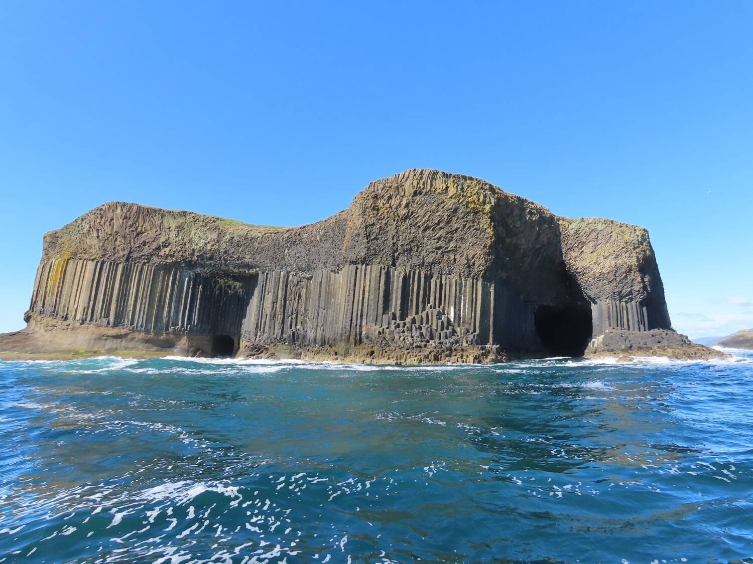 The Isle of Staffa seen from the sea on a very sunny day. The camera looks towards the basalt columns surrounding Fingal's Cave.