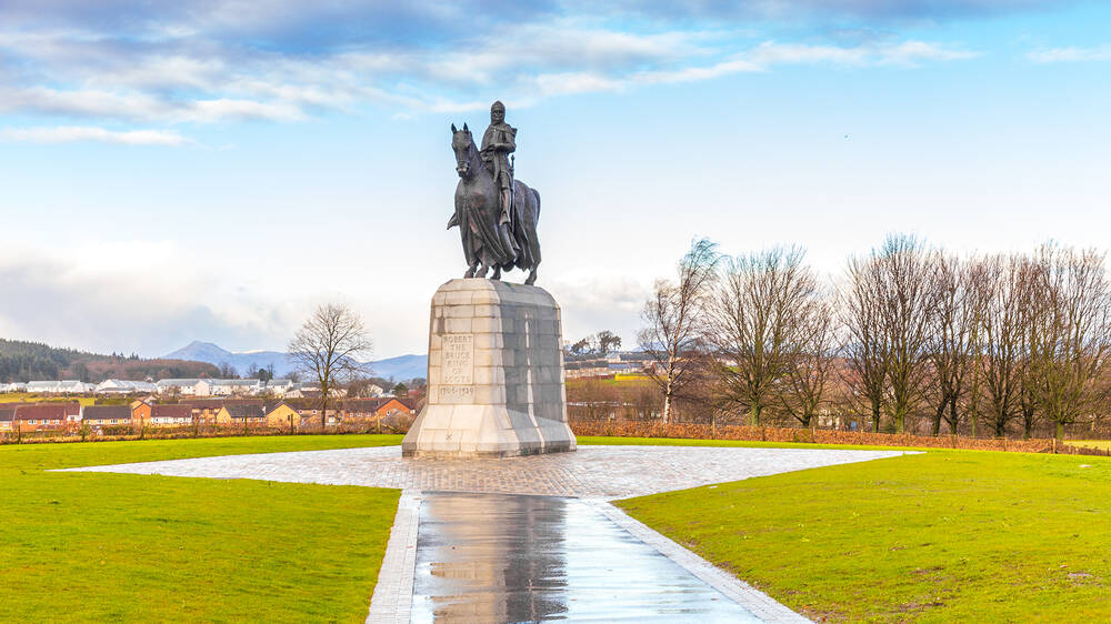 A photograph of the statue of Robert the Bruce at Bannockburn, surrounded by parkland and with a row of trees in the background.