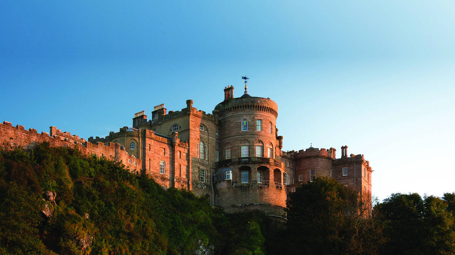 A view of Culzean Castle at dusk, with the setting sun making the walls glow red. The castle is seen from the beach below.
