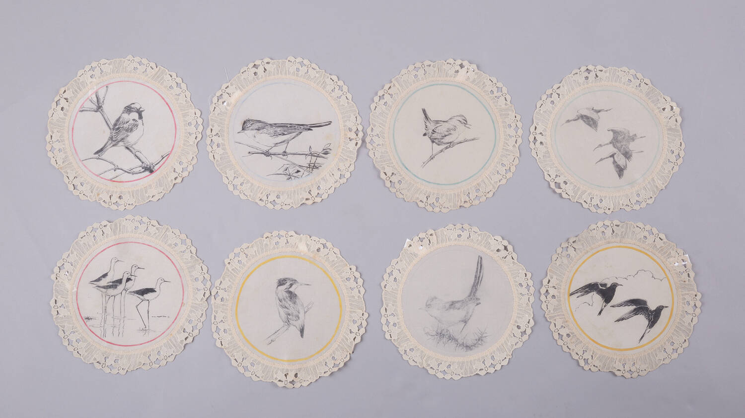 A series of 8 lace finger mats are displayed. Each contains a hand-painted black and white bird illustration.