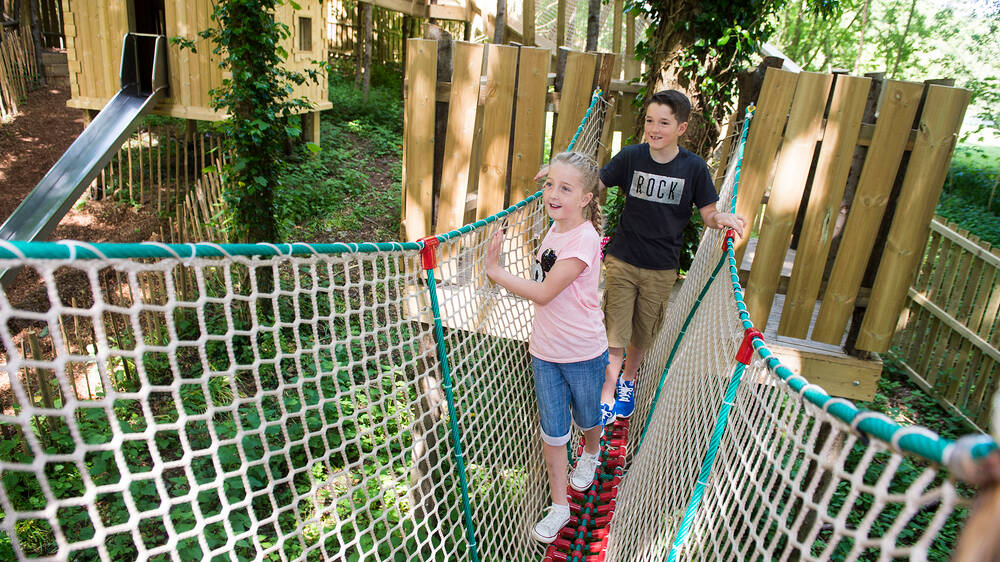 Two children on a walkway with rope netting at either side, in an adventure playground.