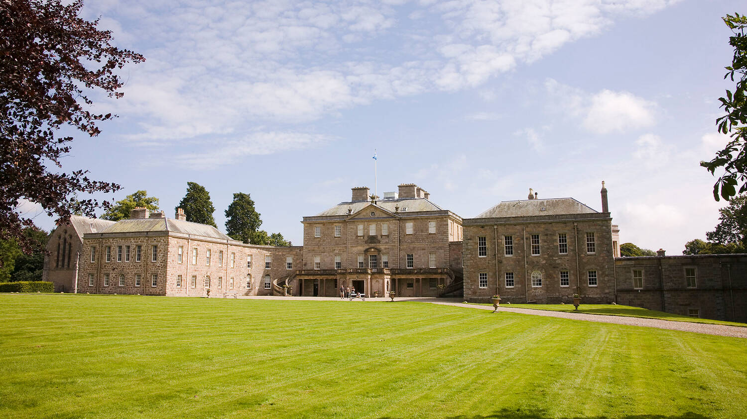 A view of a very large country house, seen from across a very neat lawn.