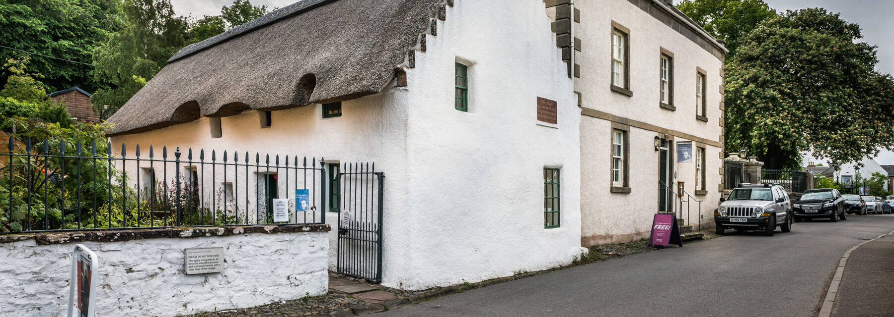 A view of an old thatched cottage, adjoining a large Georgian house.