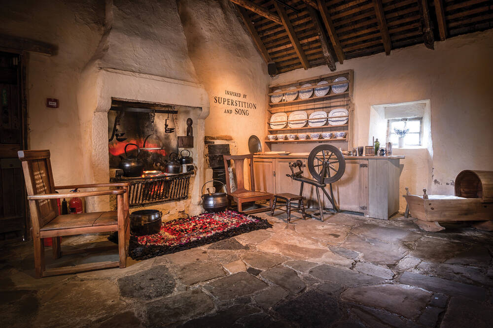 An interior view of Burns Cottage, showing the fireplace and spinning wheel.