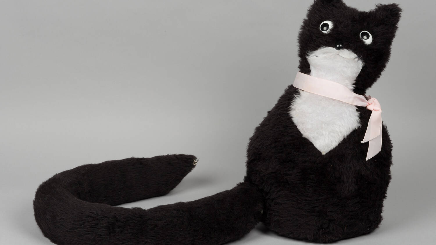 A black and white cat-shaped doorstop with a pink ribbon as a collar, and a detachable tail!