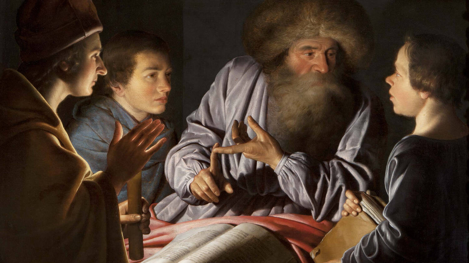 A painting of a older man (with a beard and immense furry hat) sitting round a table with his younger pupils. They all look at him. An unseen light source seems to illuminate all their faces.