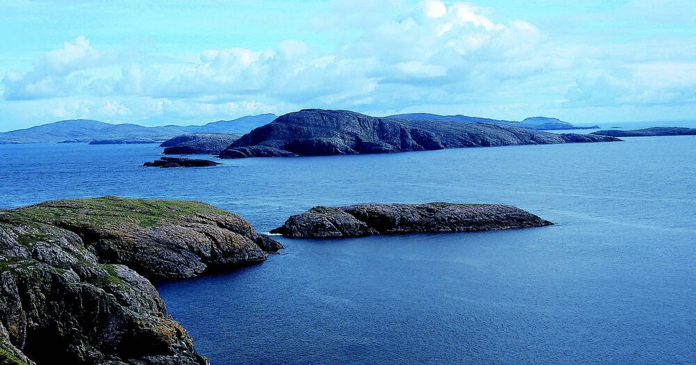 An aerial view of the island of Mingulay, surrounded by calm blue waters.