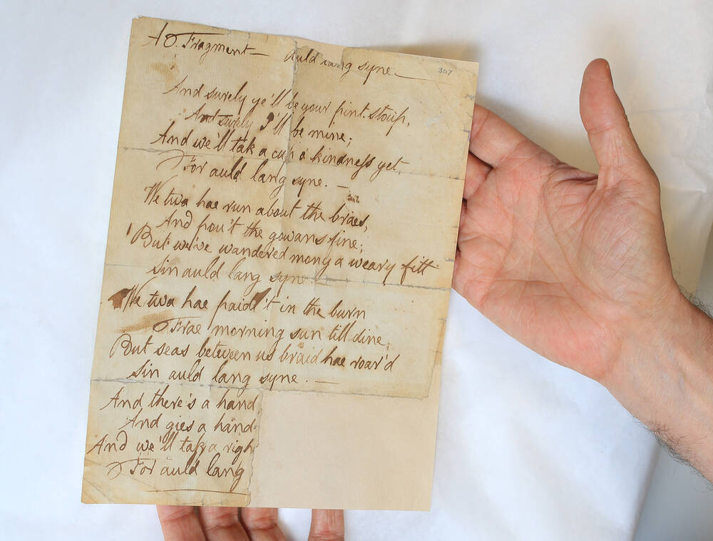 Two hands hold out a page of Burns’s handwritten manuscript for ‘Auld lang syne’.