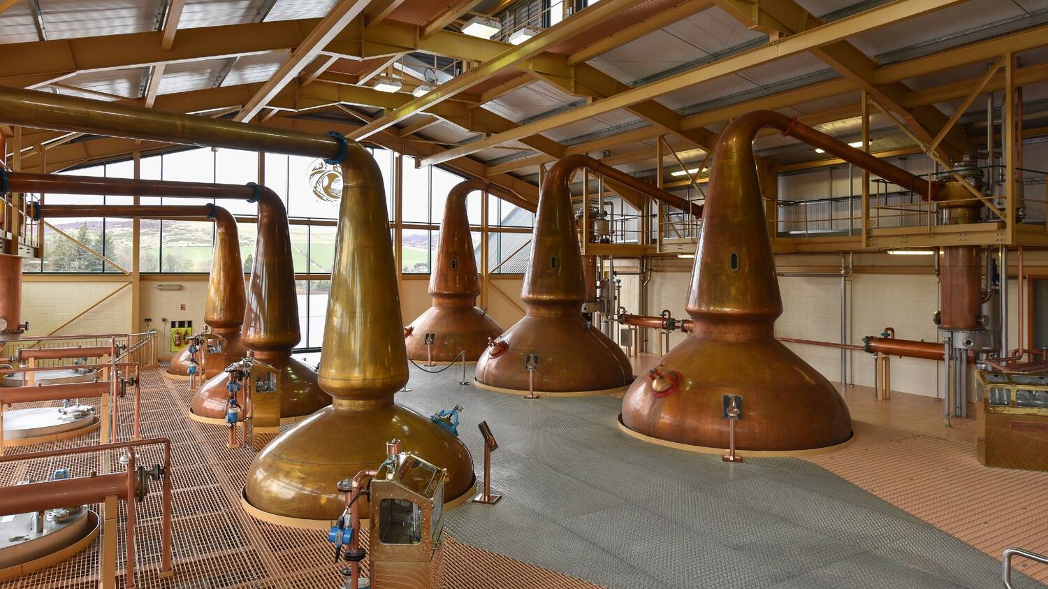 A room in a whisky distillery showing 6 large copper stills.