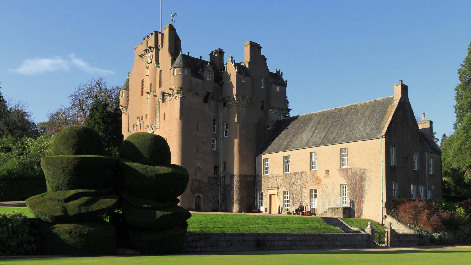 A view of Crathes Castle from the manicured lawn in front. Two large eggcup-shaped yew hedges stand in the foreground.