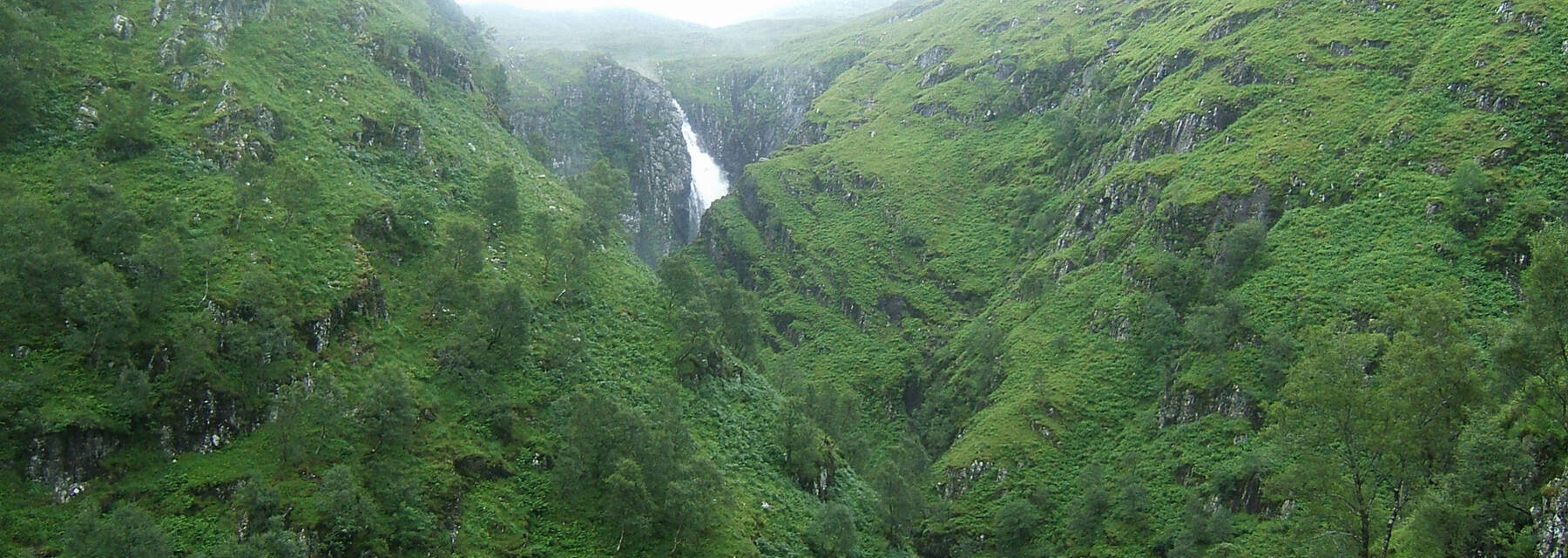 A wooded valley, with a waterfall at the far end, at Falls of Glomach.