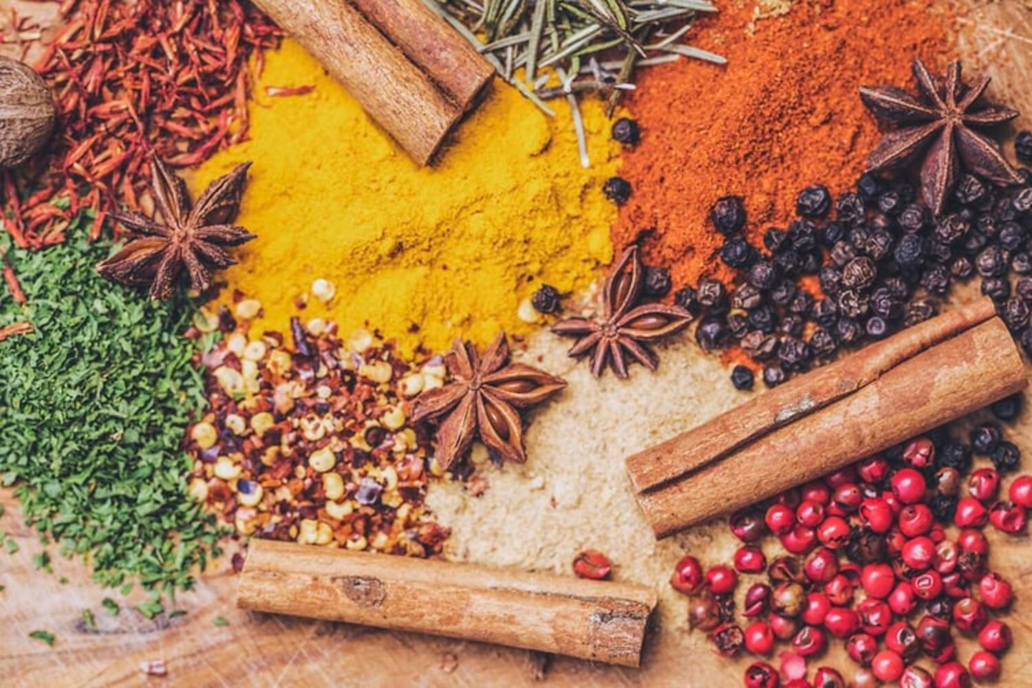 Close-up of small piles of colourful spices, including cinnamon sticks, turmeric and star anise.