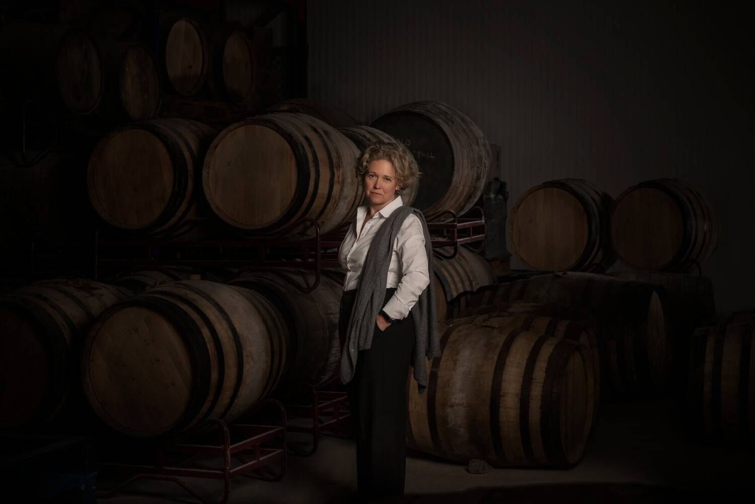 A woman is standing in front of a number of whisky barrels stored on their side.