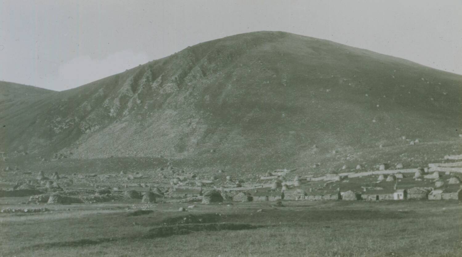 Black and white archival image of the village on Hirta, St Kilda. The large mountain of Conachair is in the background.