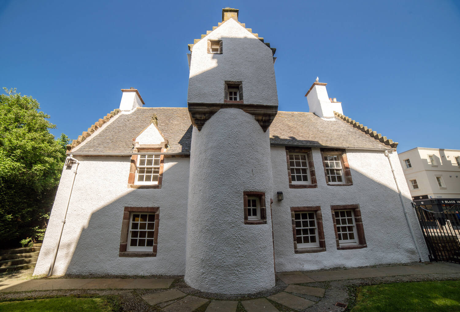 An exterior view of Abertarff House, where its bright white stone walls contrast against a deep blue sky. It has a round tower with a turreted top in the centre of the building.