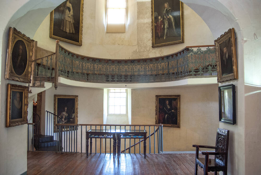 The main sweeping staircase and landing inside Alloa Tower. Large gilt-framed paintings hang on the wall.