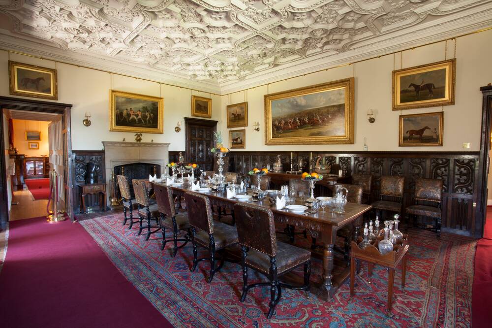 The stately dining room at Brodick Castle, with a dark-wood table and chairs to sit ten people at the centre, a stone fireplace, and walls lined with gold-framed paintings.