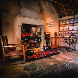 Inside the kitchen at Burns Cottage, with a traditional range at the fire and a spinning wheel to the side.