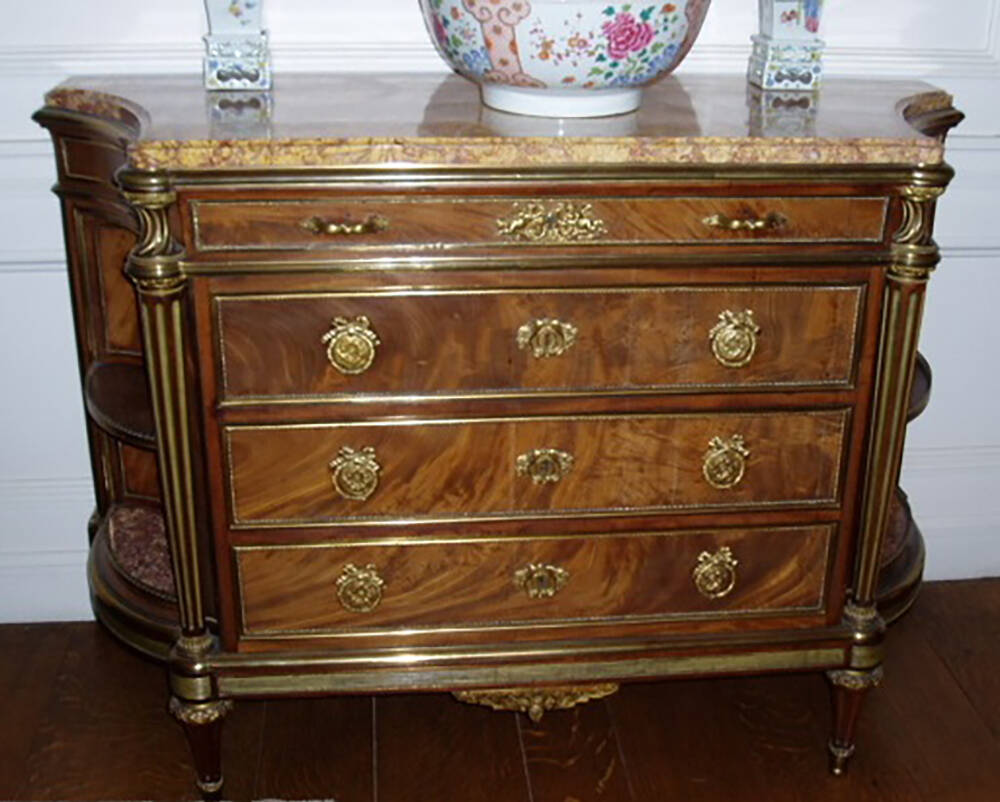 A highly polished wooden commode with four drawers at the front. A porcelain bowl and two matching vases sit on top of the cabinet.