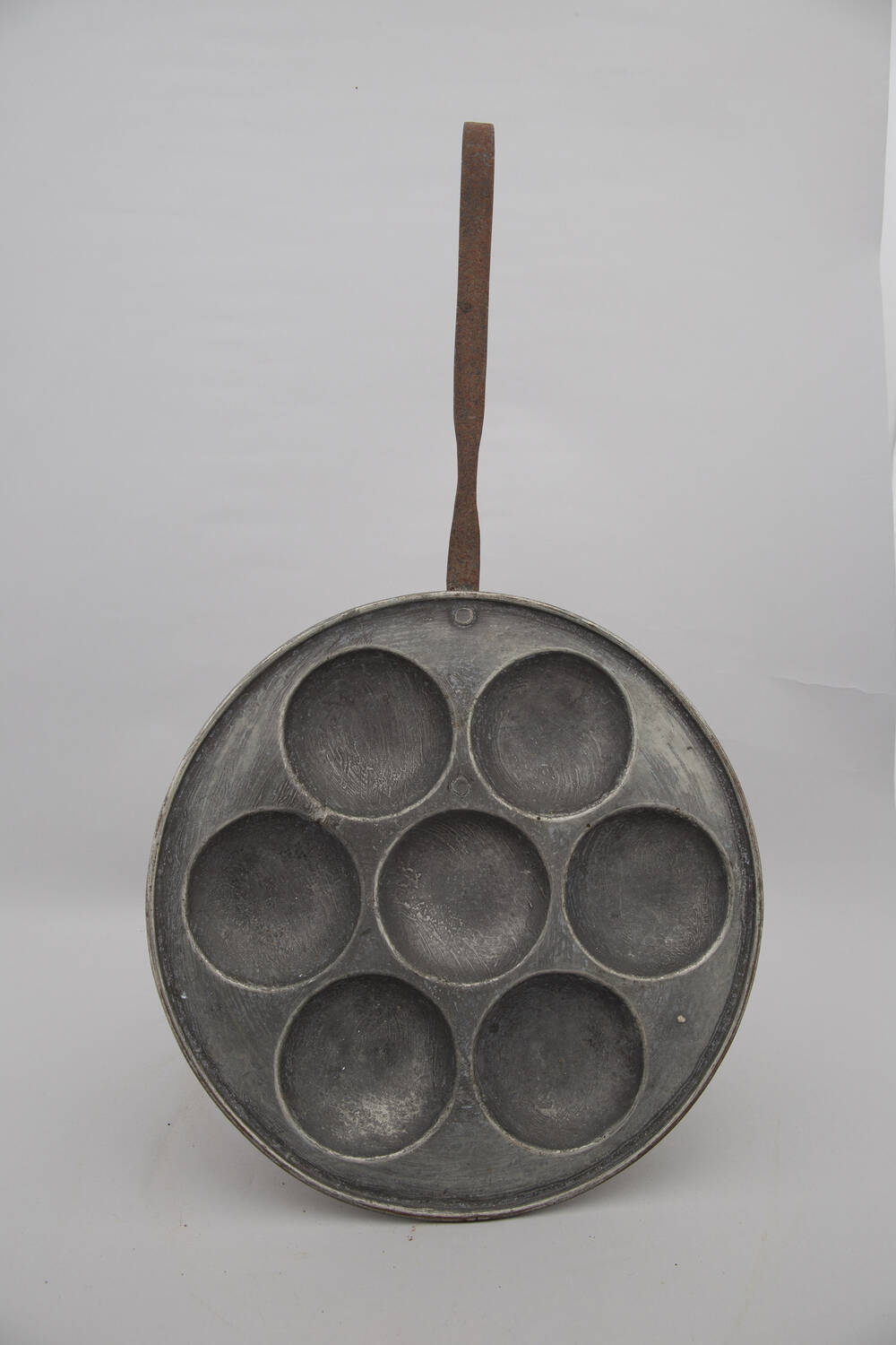 A circular metal pan that looks a bit like a frying pan, except that it has 7 round indentations in the pan.