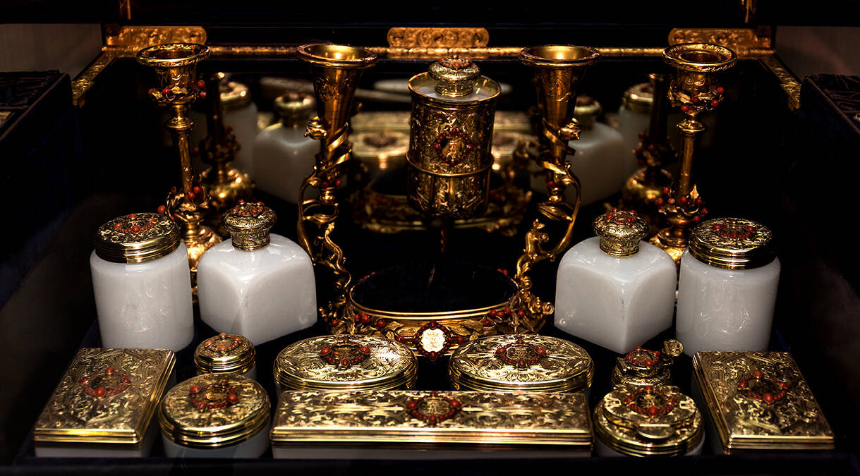 A very elaborate and ornate dressing case, filled with ceramic pots and gilt slim cases. Many of the lids are encrusted with red jewels.