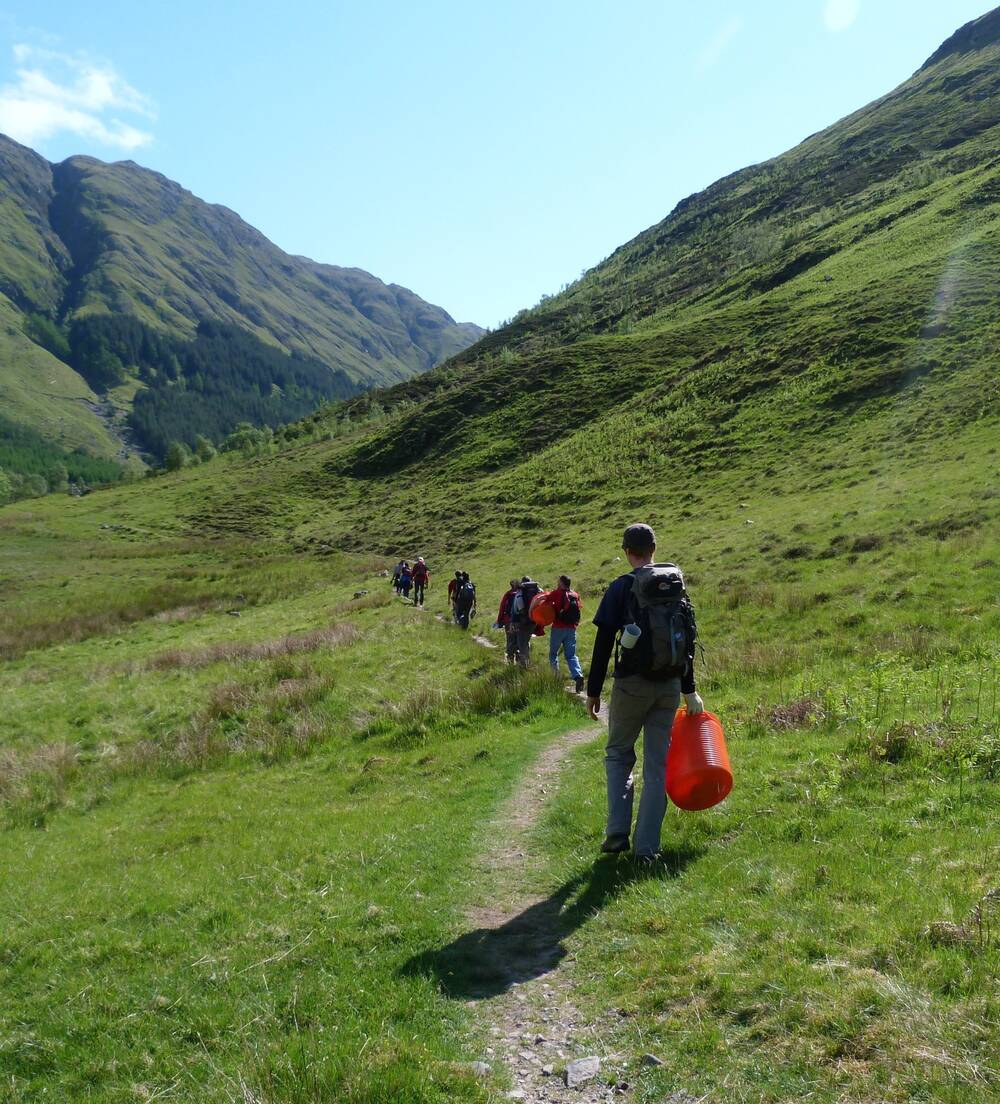 A group of volunteers walk towards their work site in Glencoe, carrying orange plastic pails.