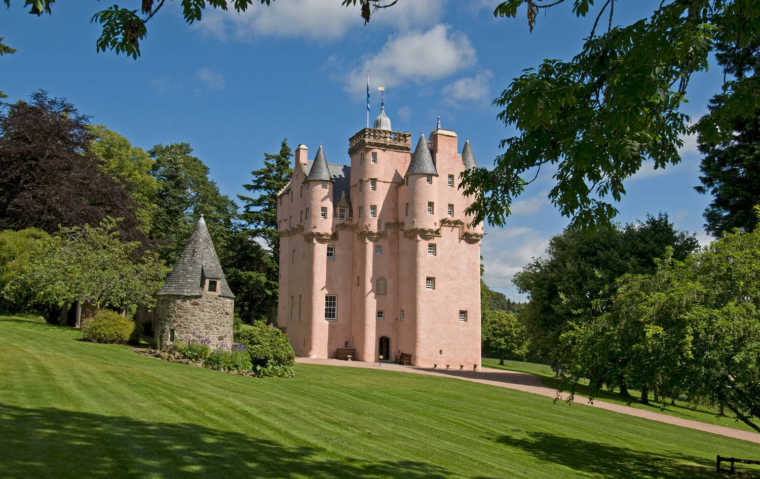 Craigievar Castle, a pink castle with turrets surrounded by a grassy lawn, with trees in the background.