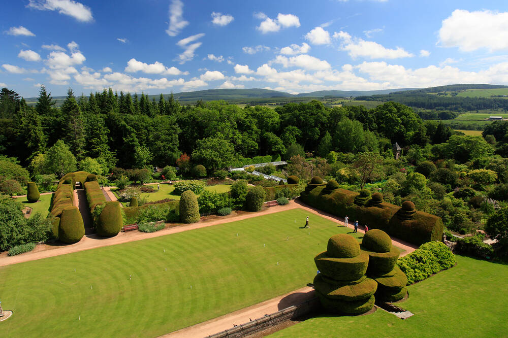 An aerial view of the lawn, walled garden and surrounding woodland at Crathes Castle. The topiary yew hedges stand out beside the lawn.