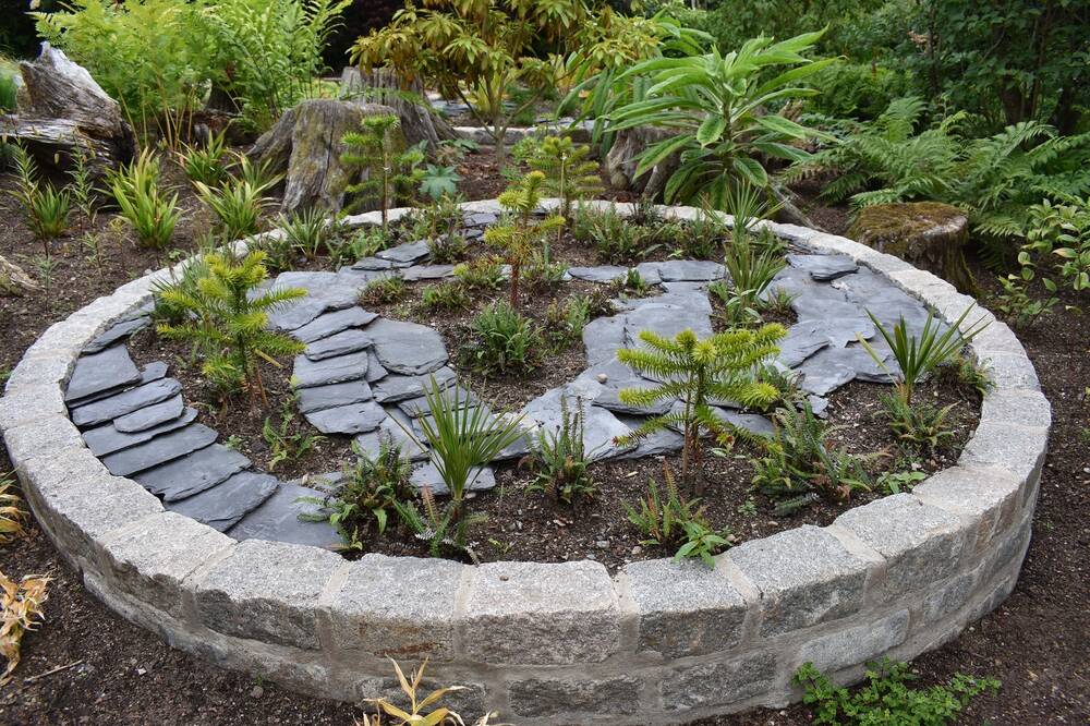 A new raised circular flower bed stands in a garden. New plants are inside it, forming the shapes of the African and American continents. They are surrounded by slate tiles to represent the oceans.