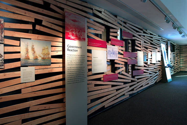 An interior view of Culloden visitor centre, showing a corridor with information panels on the walls. The walls are made from blocks of wood that appear jumbled and out of line, with gaps between them.
