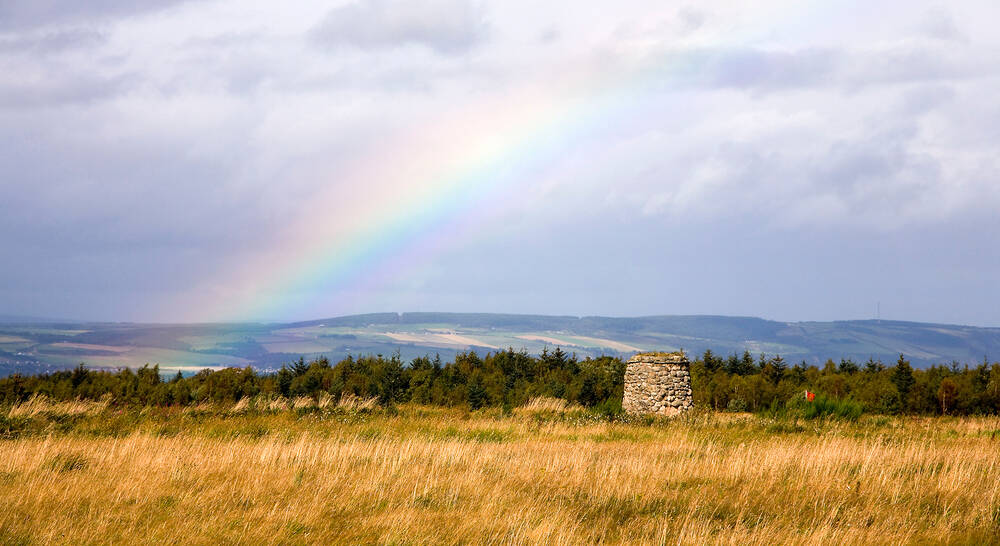 Culloden Battlefield with a rainbow forming over the top of the memorial cairn.