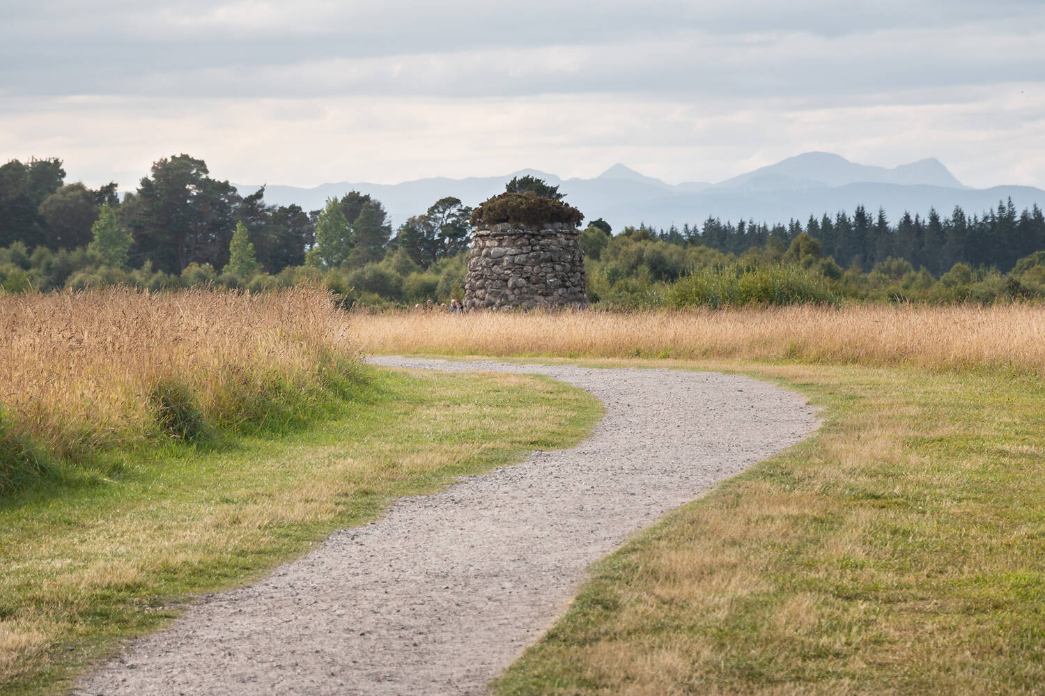 A view of the large, stone memorial cairn at the centre of Culloden battlefield. A wide stone track leads up to it across the moor.