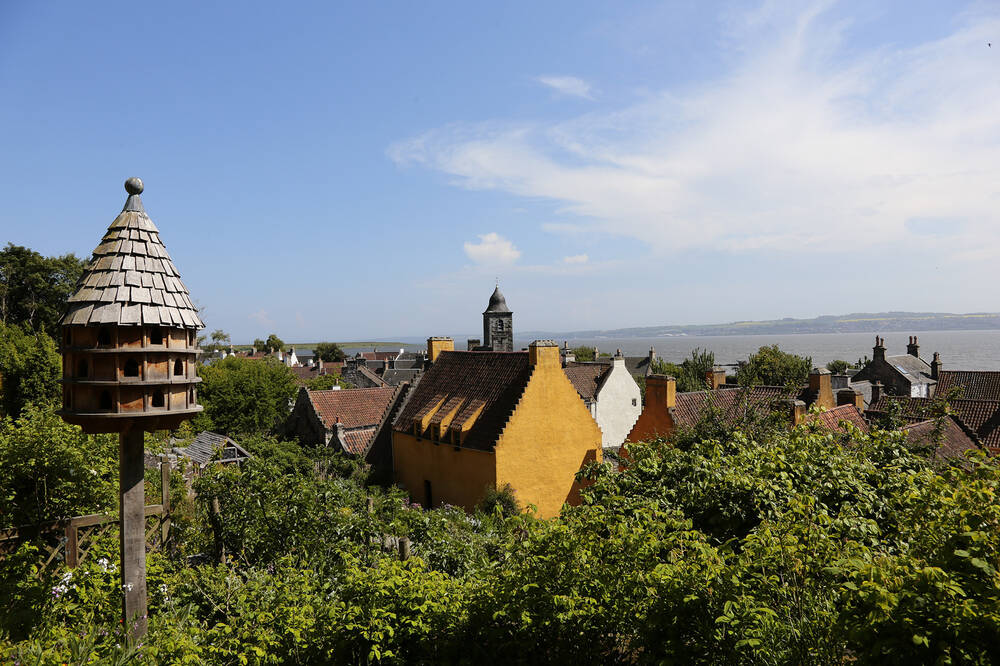 A view of the garden at Culross Palace from the high terrace, looking down across the tops of the shrubs and rooftops in the village. A tall doocot stands at the left of the image.