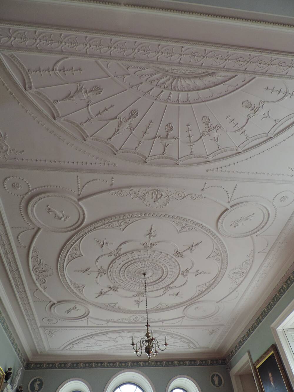 A close-up of the detail on a very decorative, white, plaster-style ceiling. A candelabra-style light hangs from the centre of the ceiling.