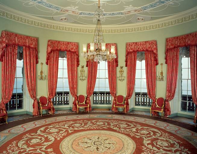 The Round Drawing Room at Culzean Castle, with a number of windows looking out over the Firth of Clyde. A large red patterned circular carpet covers the floor.