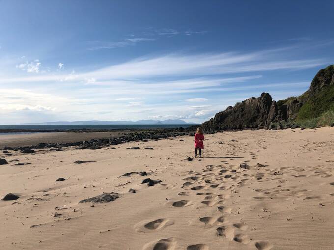 A young girl walks on the vast sandy beach at Culzean Castle on a sunny day.
