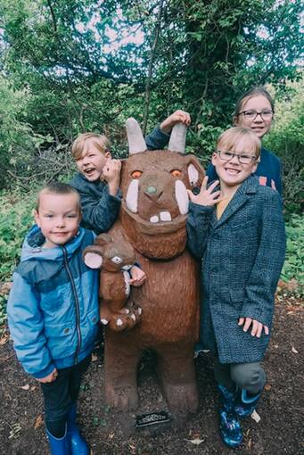Four children stand beside the Gruffalo statue in Culzean walled garden. The Gruffalo is holding the Mouse in his paw.