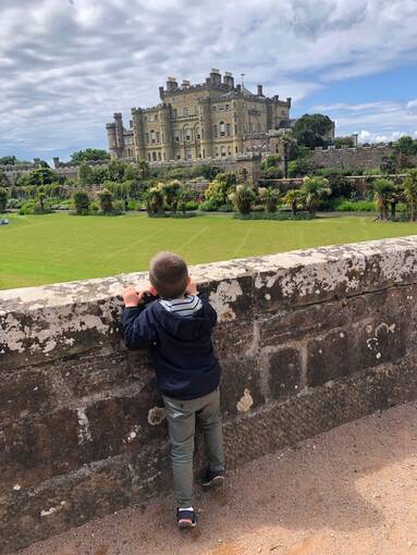A boy leans against a stone wall and looks towards Culzean Castle in the background.