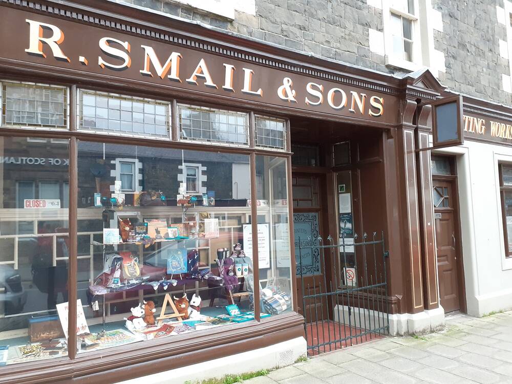 An image of a Victorian-windowed shop front with R. Smail & Sons in gold letters above the window. The door to the shop is on the right.