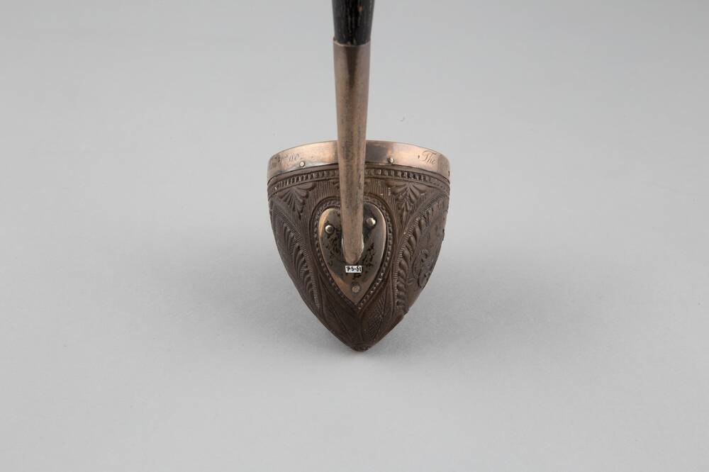 A view of the reverse of a wooden ladle, showing the join to the silver handle. A small white label is positioned just below the handle joint.