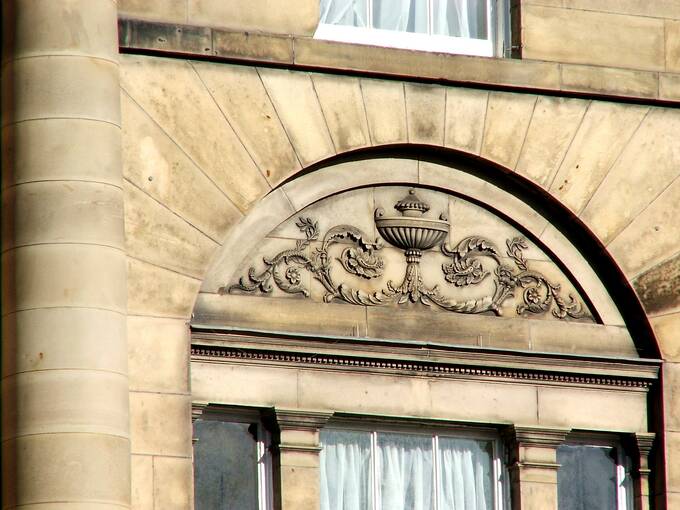 An urn and classical flourishes are carved into the stone arch above a window.