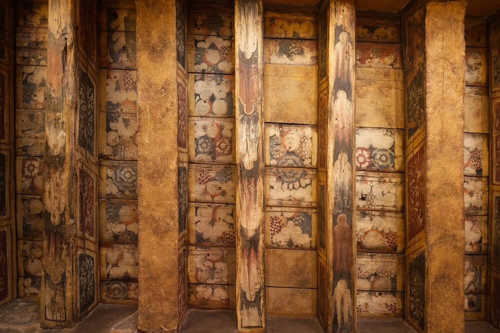 A close-up view of decorated wooden beams, forming part of a ceiling. Images of fruit and flowers can be seen.