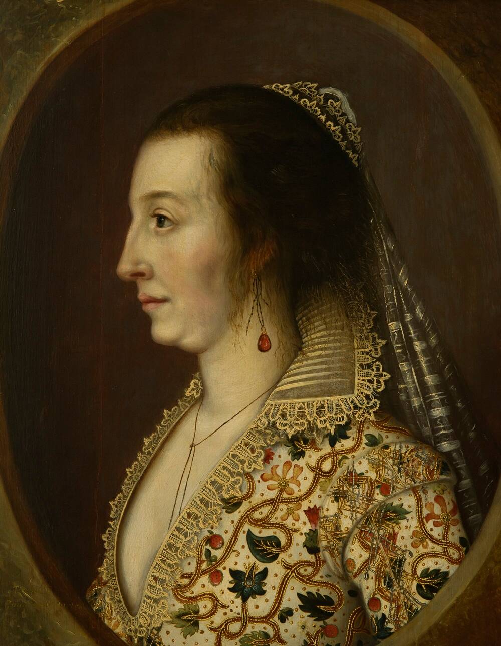 An oil painting of a 17th-century woman, showing her top half. She is smartly dressed in an embroidered jacket with a stiff lace collar. She wears a light veil in her hair and drop pearl earrings.