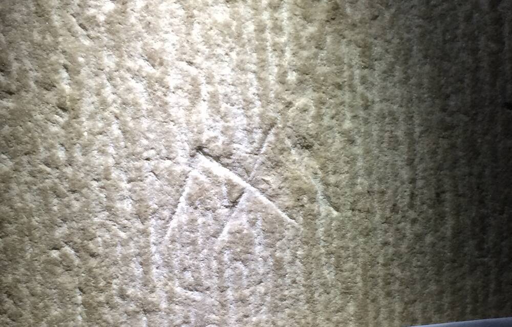 A close-up view of a stone wall with two etched marks upon it, in the shape of a capital M.