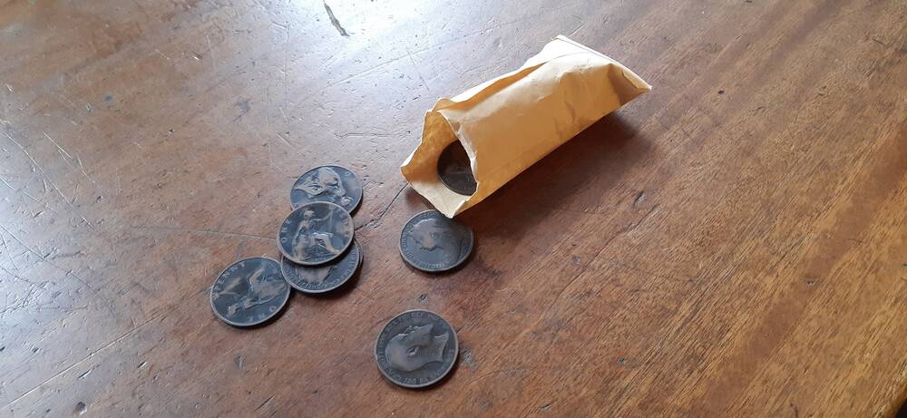 An envelope of old pennies spilling onto a wooden desk.