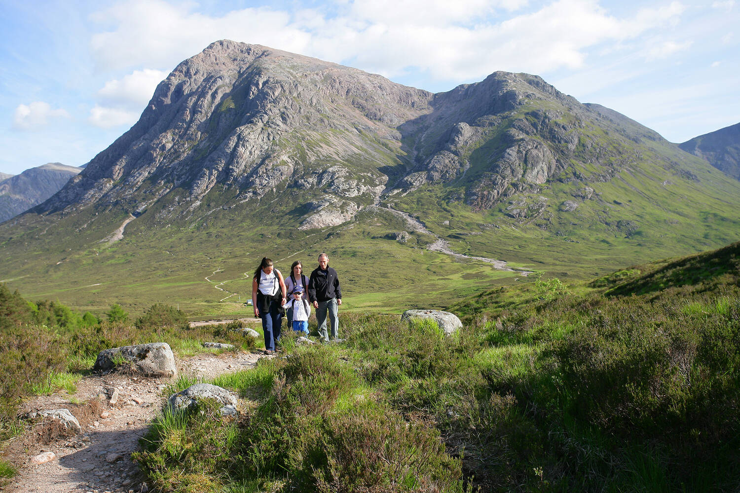 A family of two adults and two children walk along a path in Glencoe with Buachaille Etive Mor in the background.