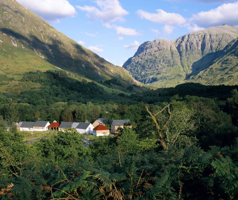 A view of the Glencoe Visitor Centre seen from above, surrounded by trees and nestled beneath towering mountains.