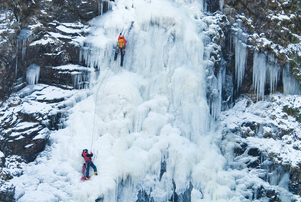 Two ice climbers use ropes to make their way up a frozen waterfall.